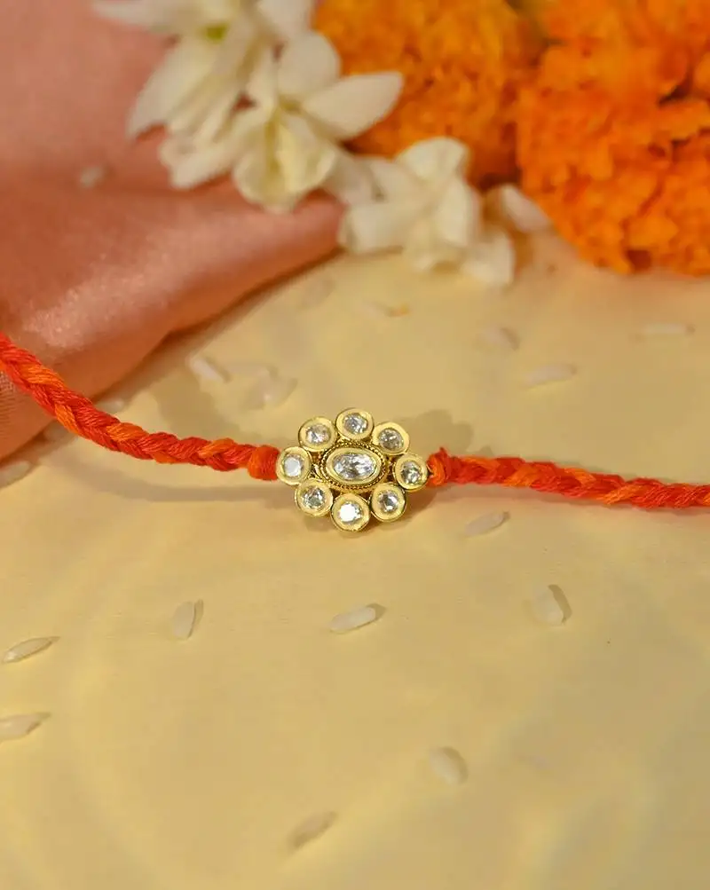 Orange thread floral rakhi with shimmering stone centrepiece