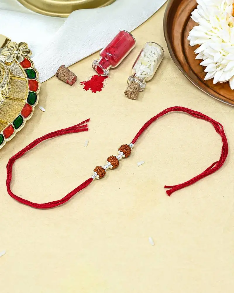 Red thread rakhi with three rudraksha beads and silver accents